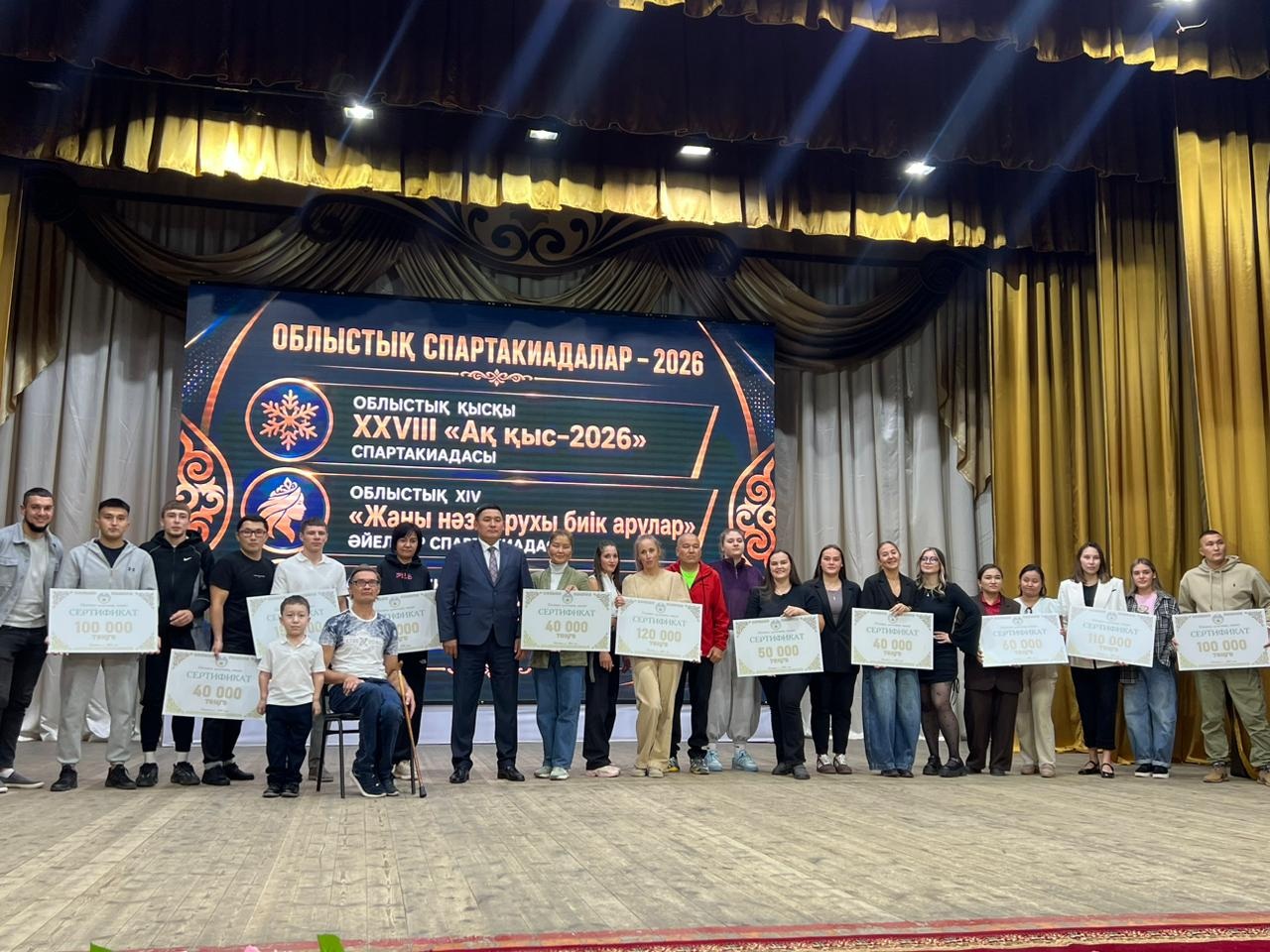 Облыстық спартакиада жеңімпаздарының сыйлық сертификаттарымен сахнадағы топтық суреті.