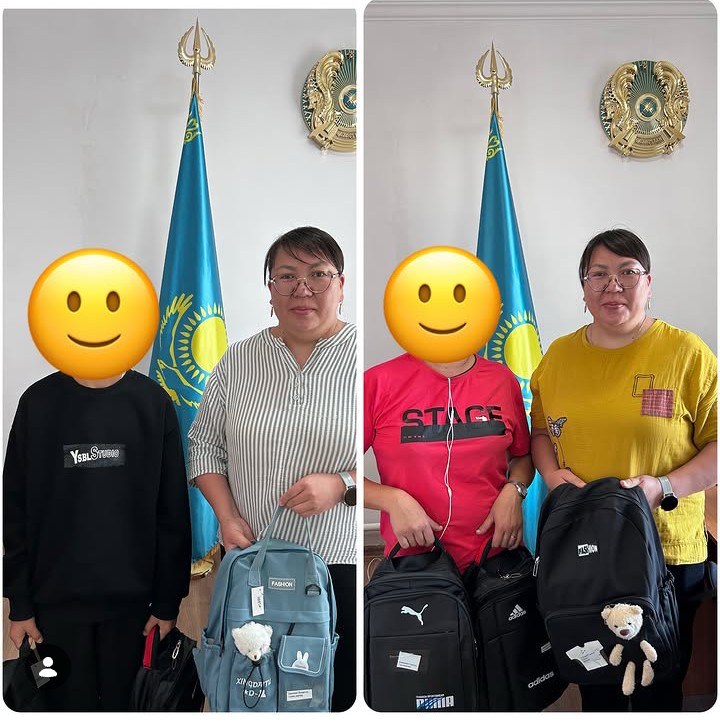 Қазақстан туы мен гербінің алдында тұрған екі адам және олардың қолындағы мектеп сөмкелері.