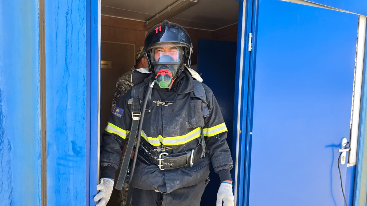 Арнайы киімі мен тыныс алу маскасы бар құтқарушы көк есіктің алдында тұр.