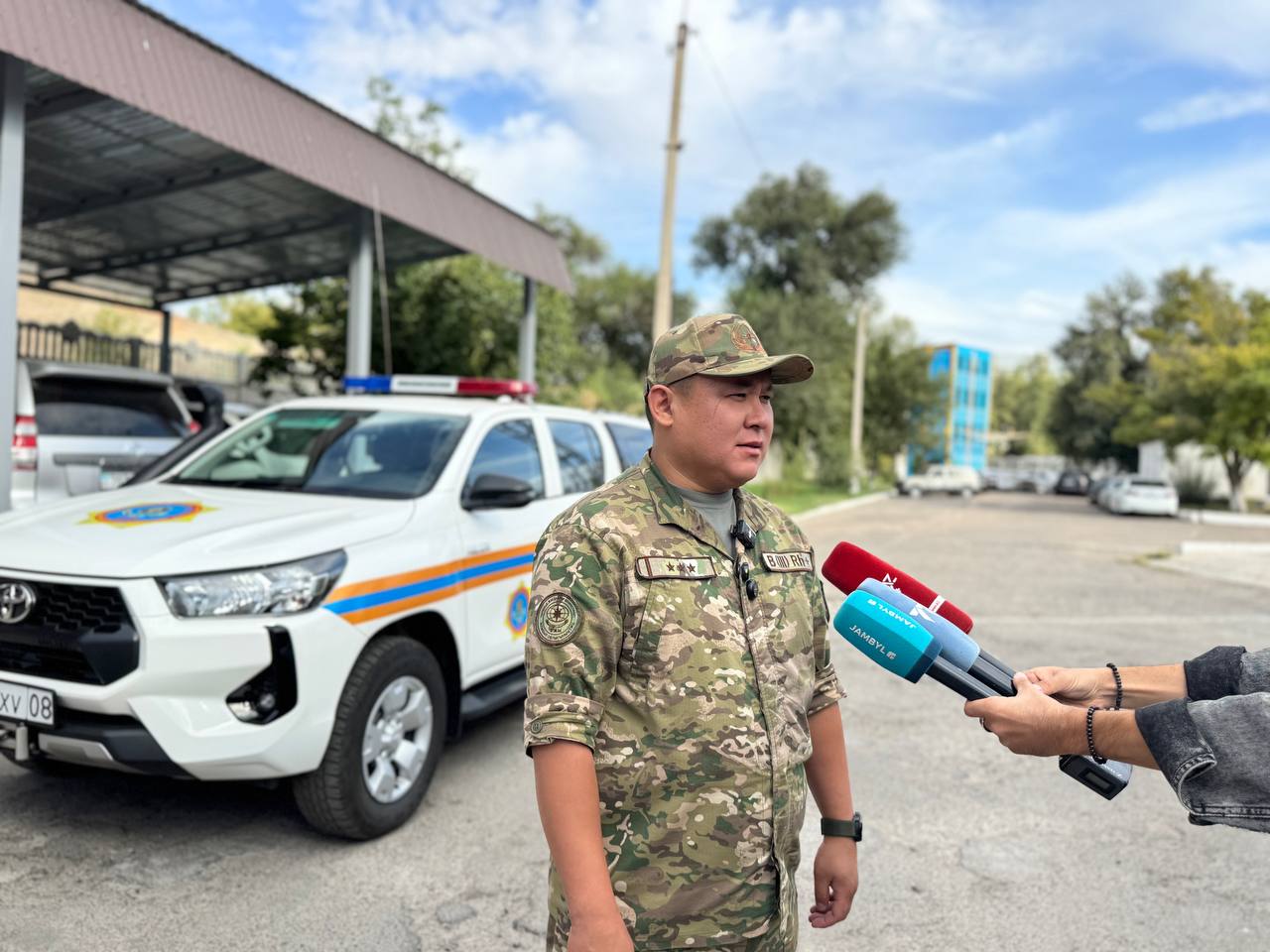 Әскери формадағы адамның полиция көлігінің жанында сұхбат беруі.
