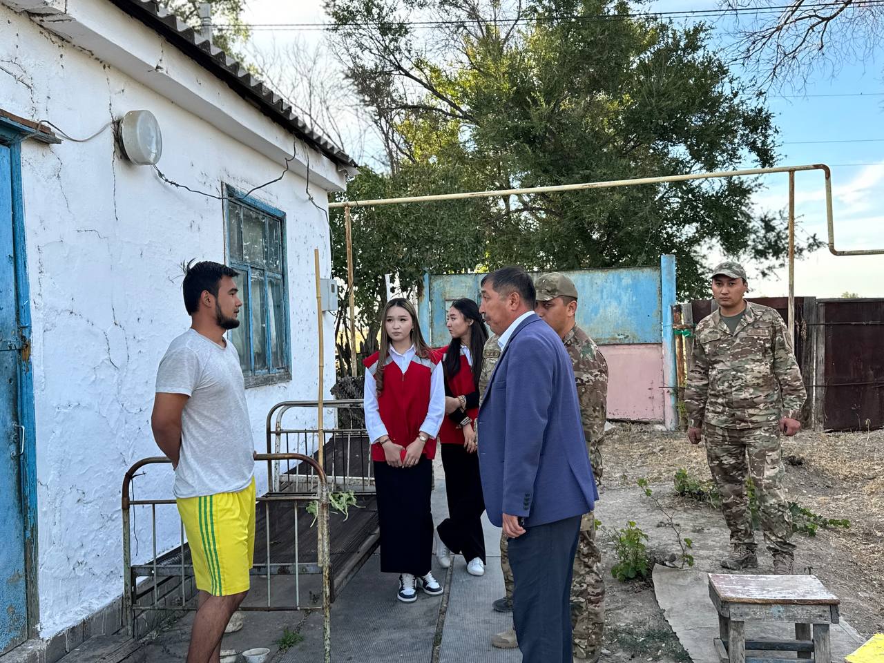 Үйдің алдында тұрған ресми киінген адамдар мен әскерилердің тобы.