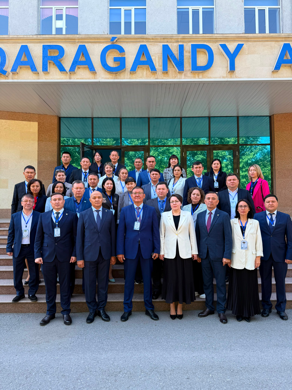 Групповое фото людей в деловой одежде на фоне здания с надписью «QARAGANDY».