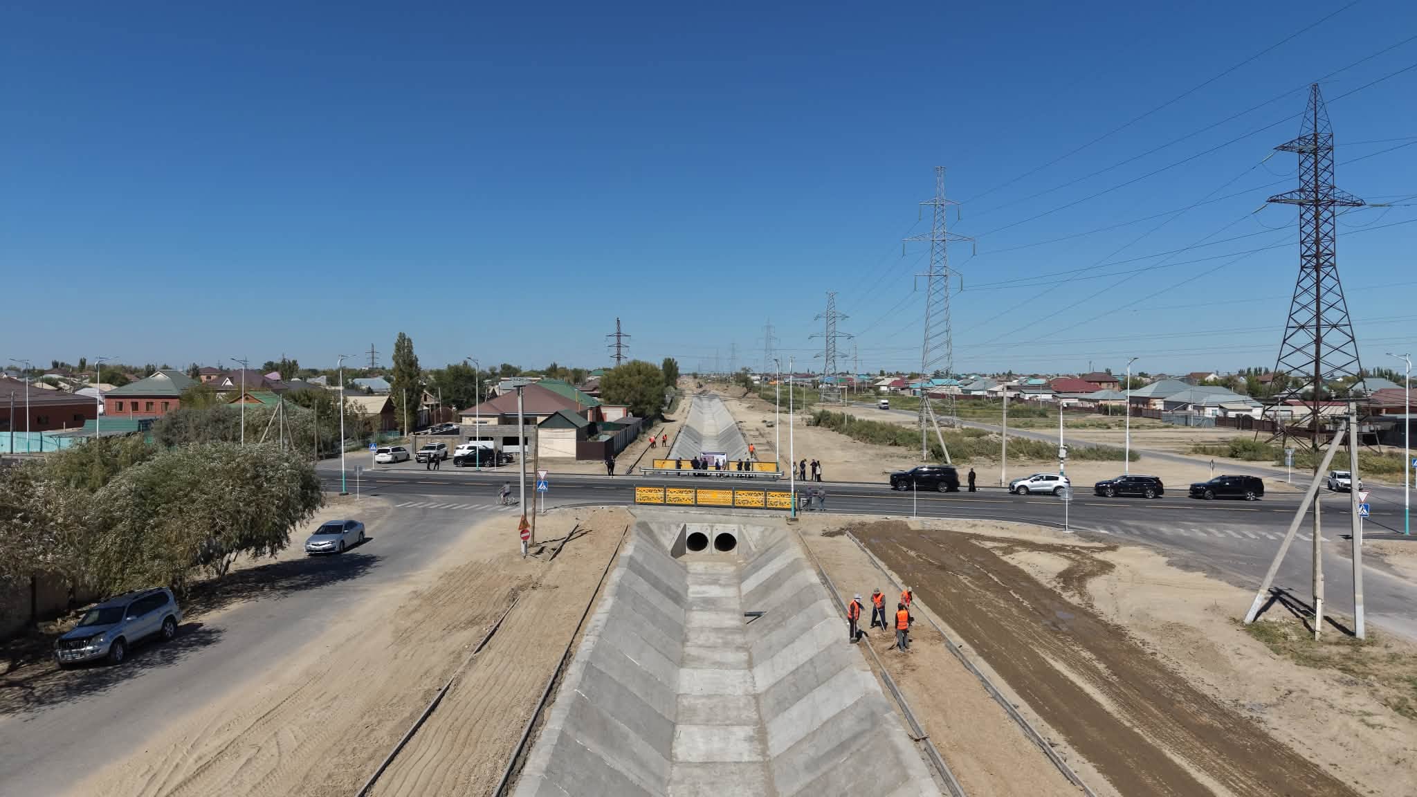 Қала шетіндегі бетон сутөгіш арнасы және жанындағы жол, электр желілері.