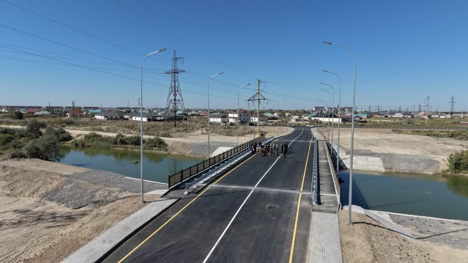 Өзен үстіндегі жаңа асфальтталған көпір және оның жанындағы адамдар.