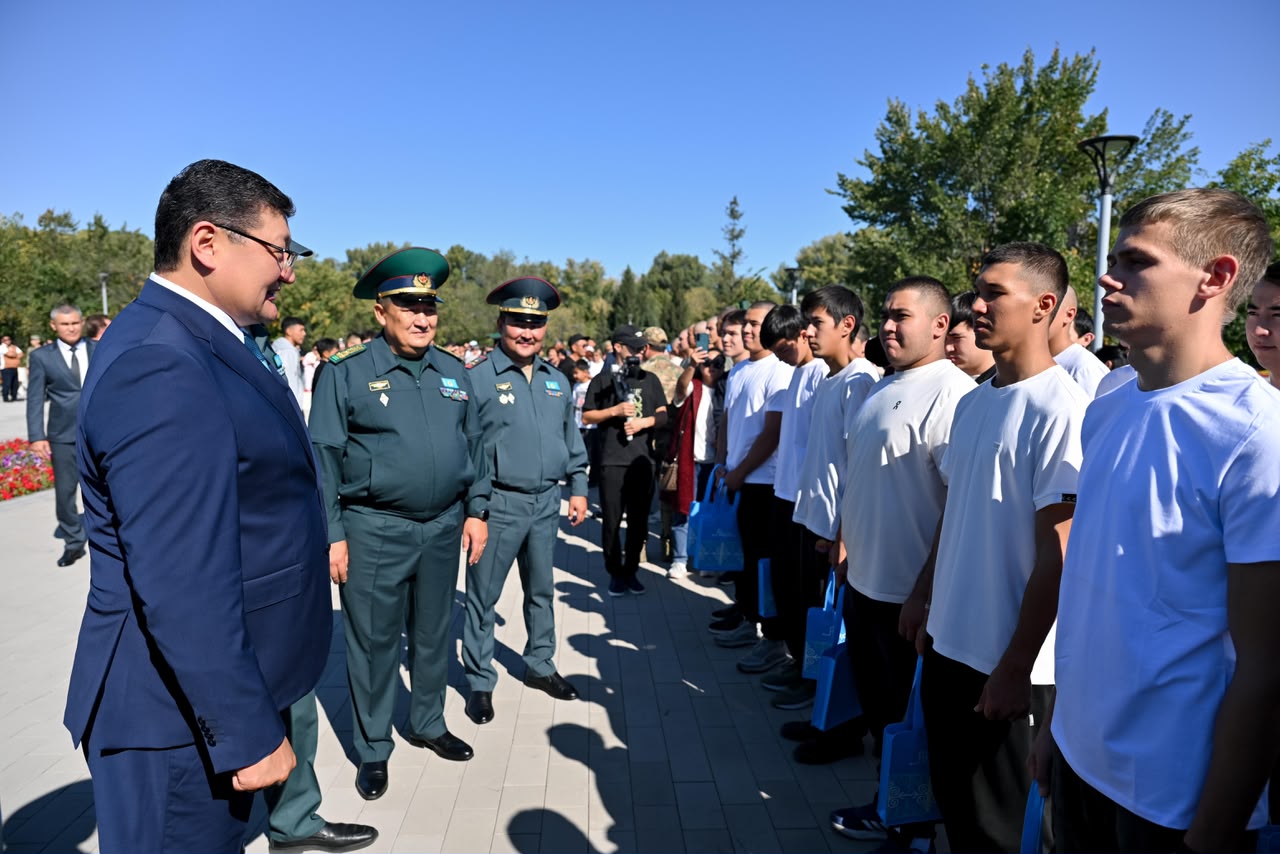Костюм киген ер адам әскери формадағы офицерлермен және ақ жейде киген жастармен кездесуде.