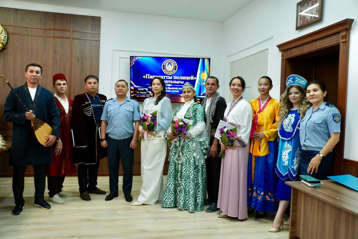 Ұлттық киімдегі және ресми формадағы адамдар тобы «Парасатты полиция» жазуы бар экранның алдында тұр.