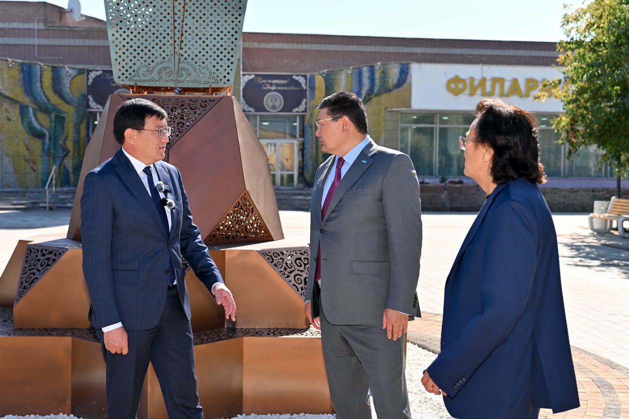 Костюм киген үш ер адамның ескерткіштің жанында тұрып сөйлесуі.