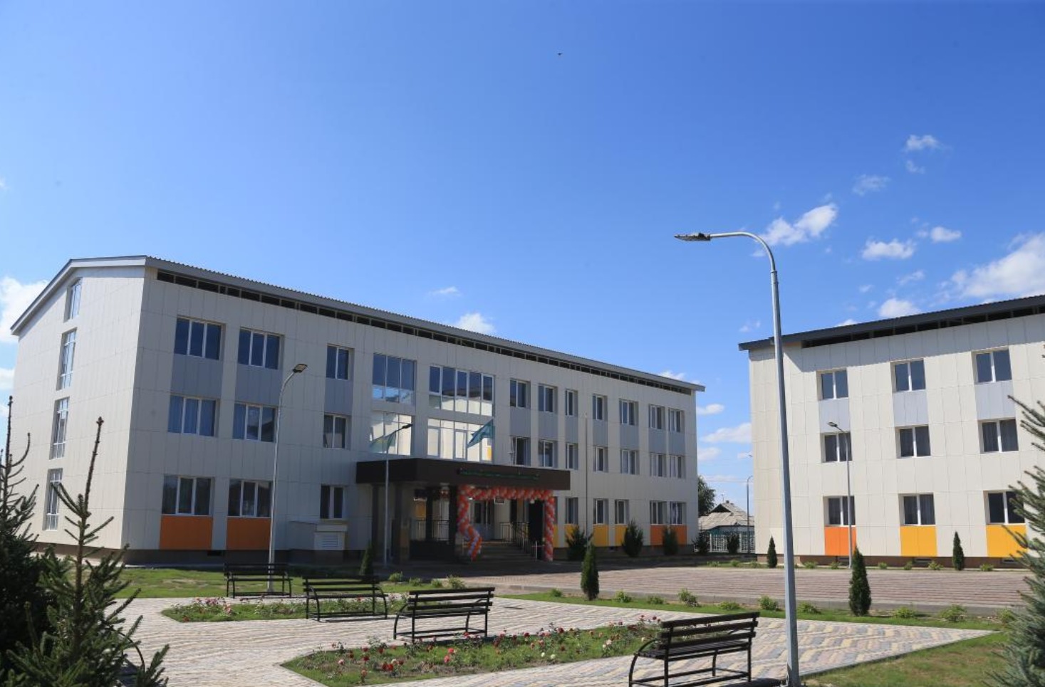 Заманауи үш қабатты екі ғимарат пен алдындағы саябақ.