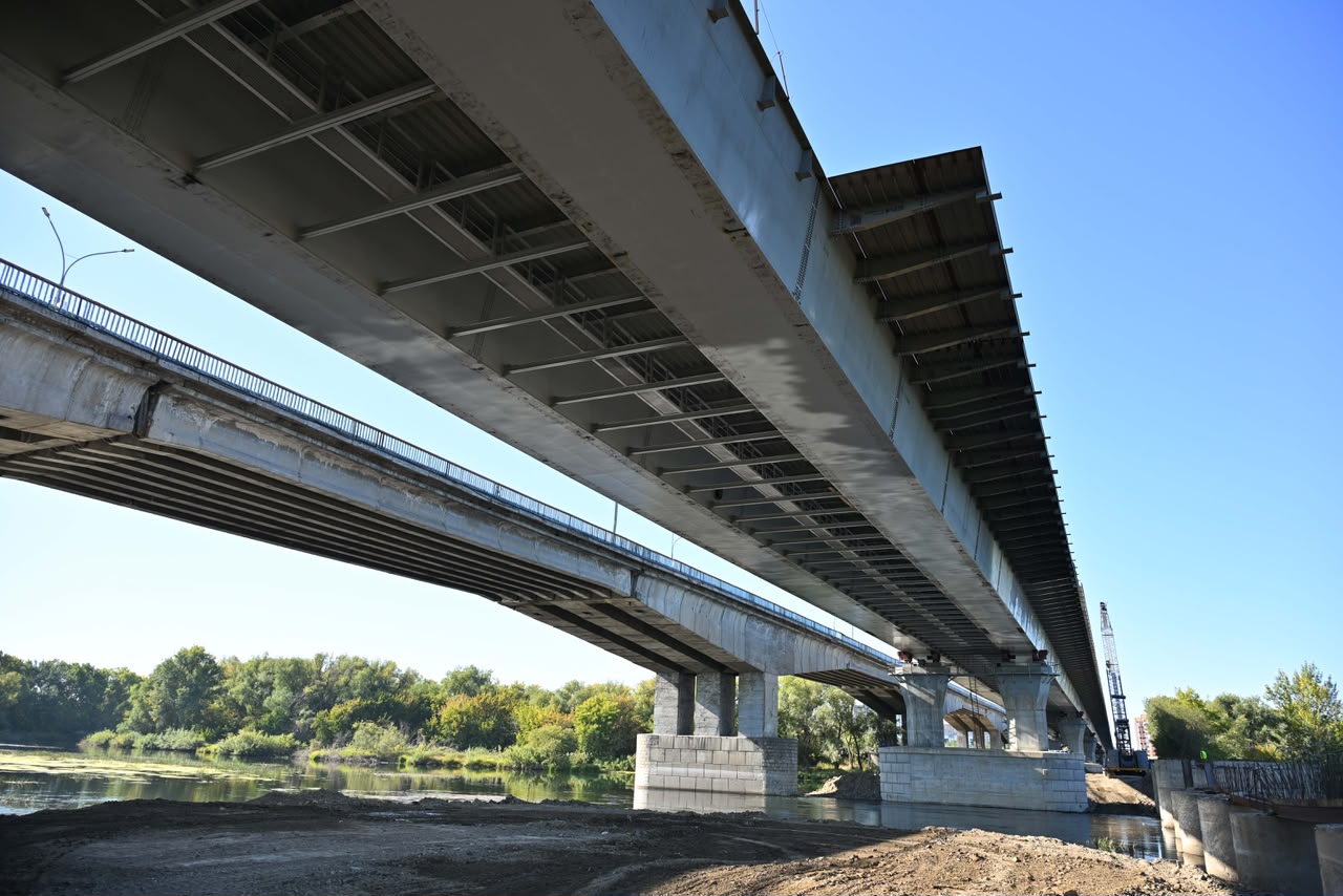 Өзен үстіндегі екі параллель бетон көпірдің төменгі көрінісі.