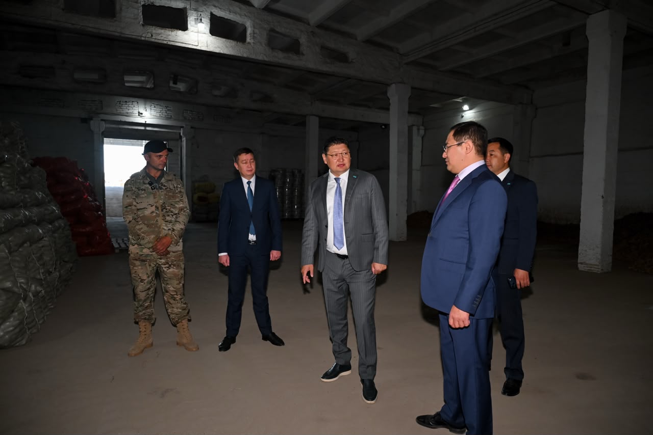 Костюм киген ресми тұлғалар мен әскери формадағы сарбаз қоймада тұрып сөйлесуде.