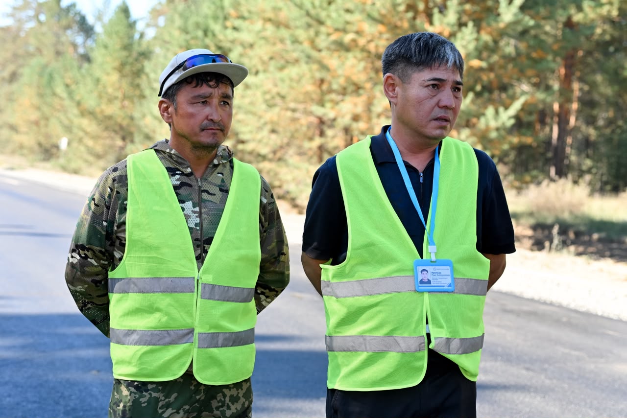 Жол жиегінде сары рефлекторлы жилет киген екі ер адам.