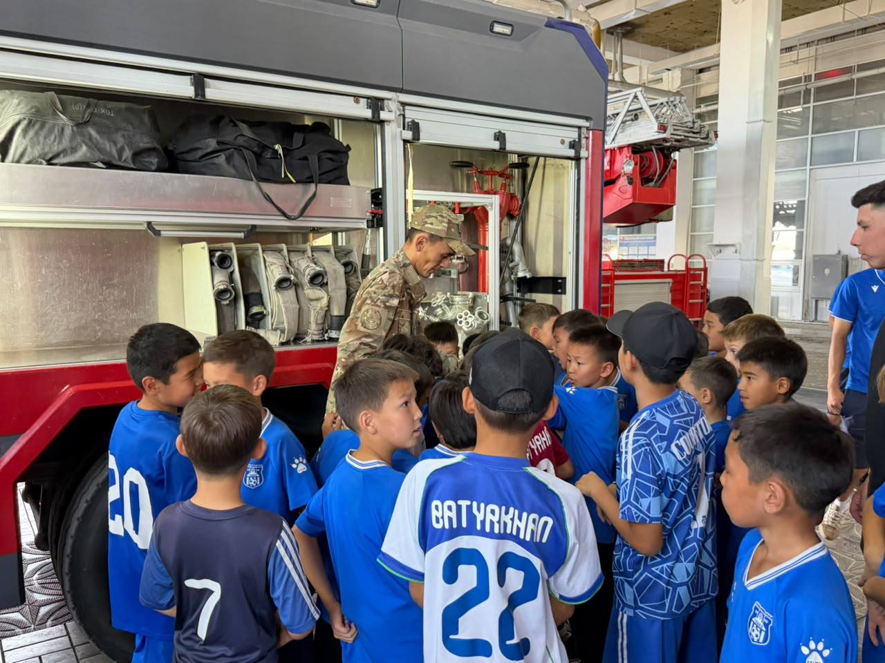 Өрт сөндірушінің көлігінің жанында тұрған көк формалы балалар тобы.