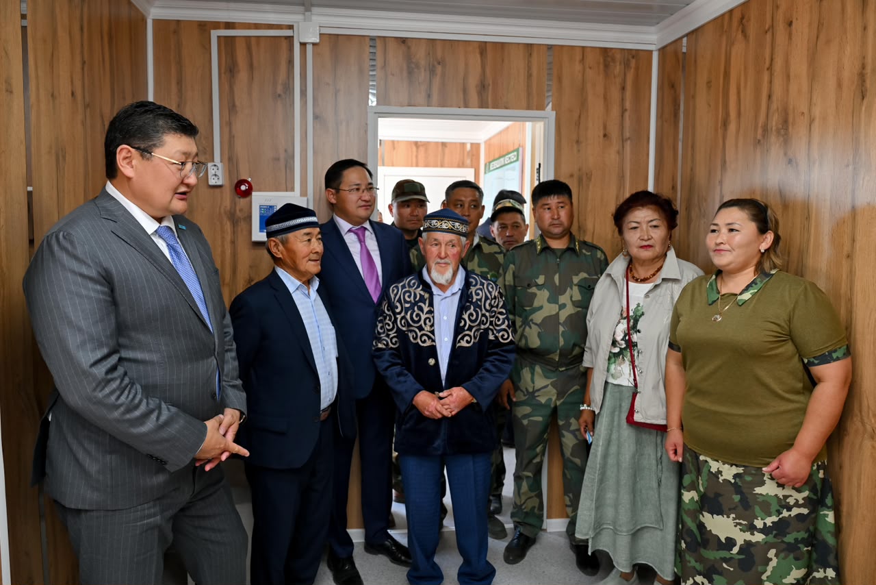 Костюм киген ер адам мен әртүрлі киімдегі адамдар тобының бөлмедегі кездесуі.