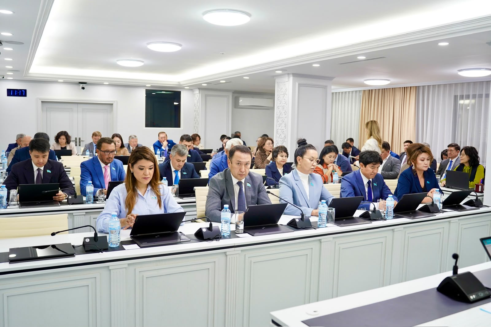 Конференция залында ноутбуктермен жұмыс істеп отырған ресми киінген қатысушылар.