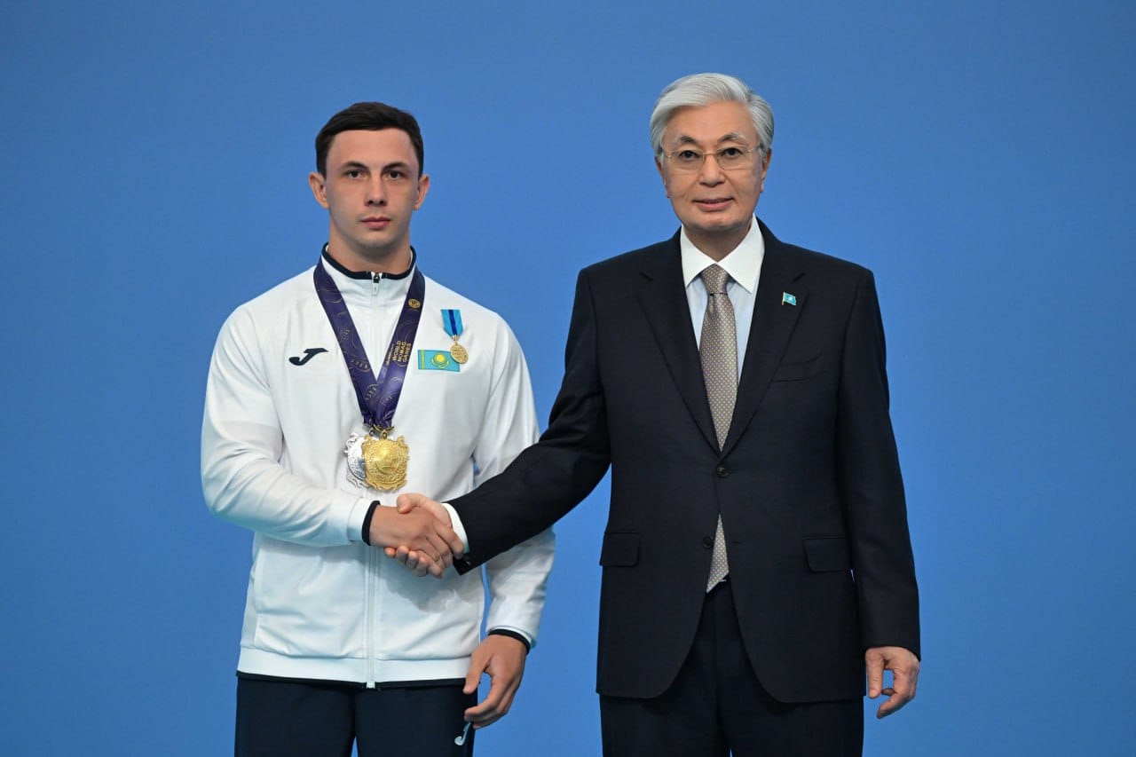 Қазақстан Президенті Қасым-Жомарт Тоқаев медаль иегері спортшымен қол алысып тұр.