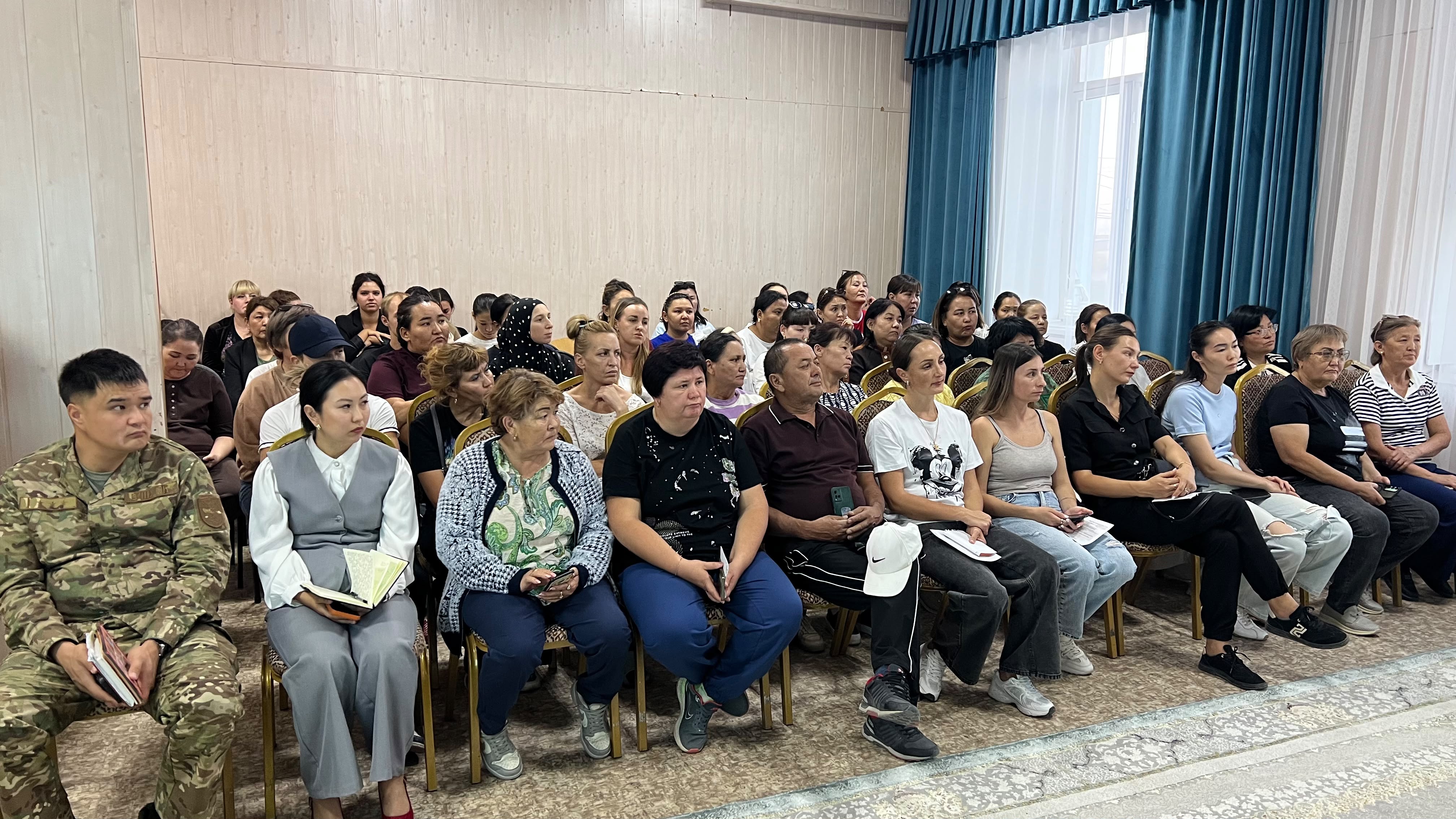 Группа людей разных возрастов сидит в зале и внимательно слушает выступление.