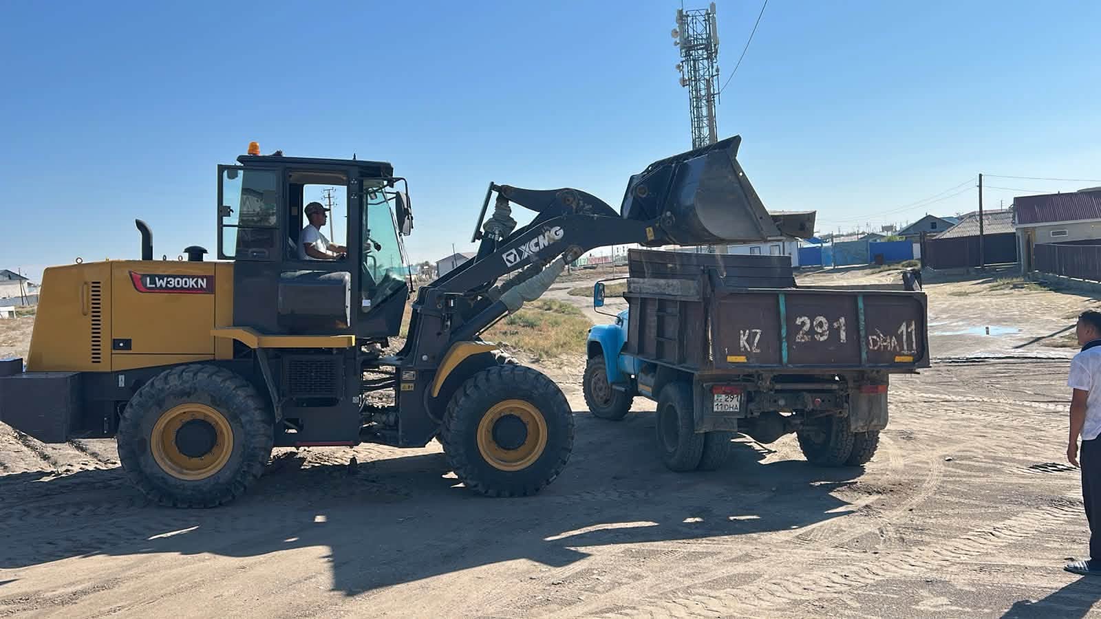 Сары XCMG LW300KN фронталды жүктегіші көк жүк көлігіне құм тиеп жатыр.