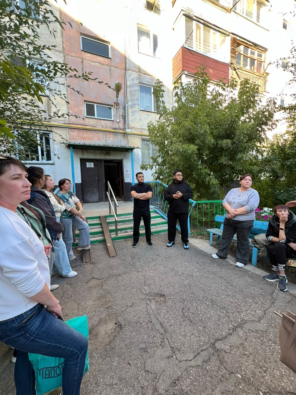 Көпқабатты үйдің алдында жиналған адамдар тобы.