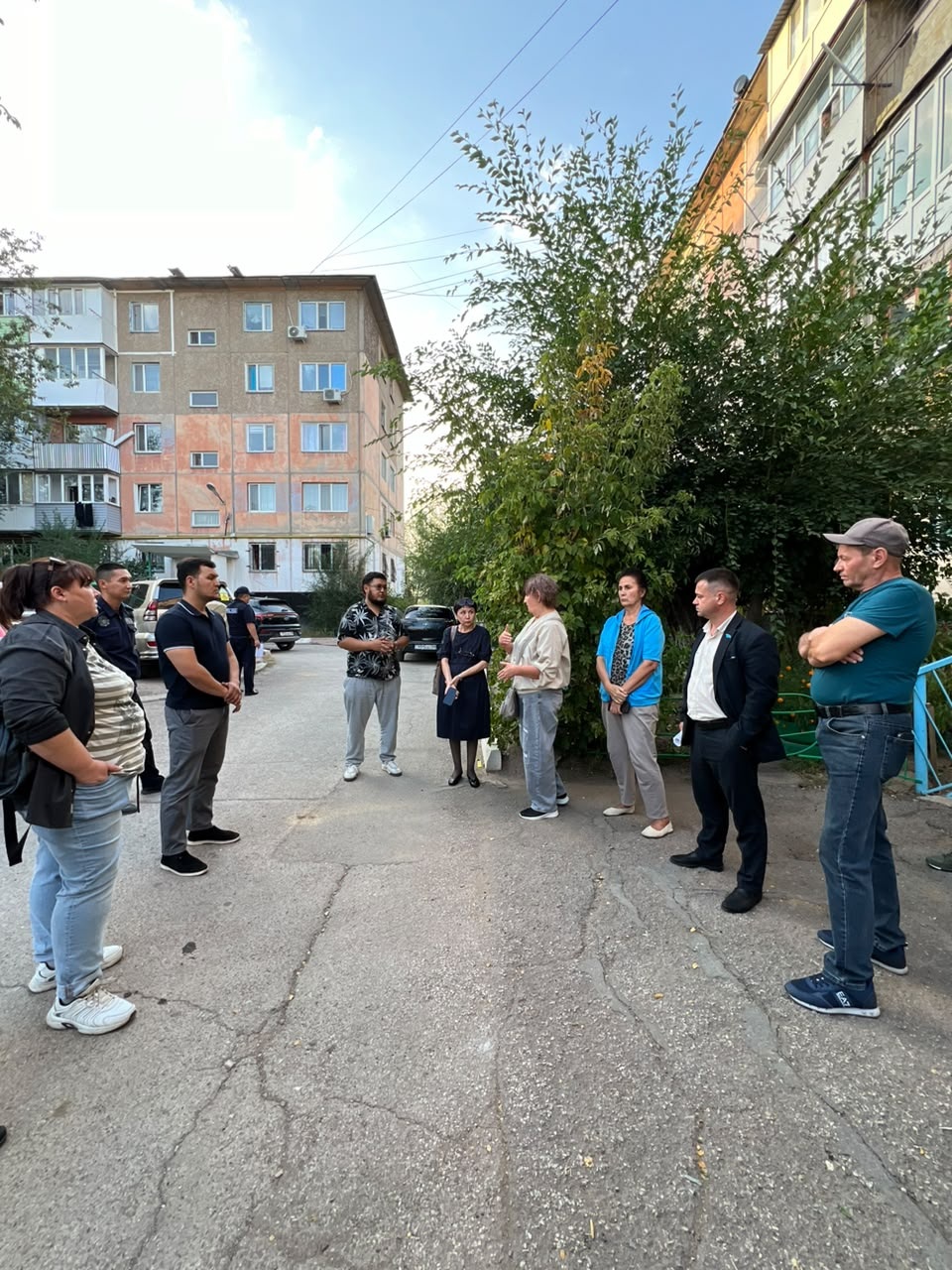 Көппәleştirмелі үйлердің ауласында жиналған адамдар тобы.