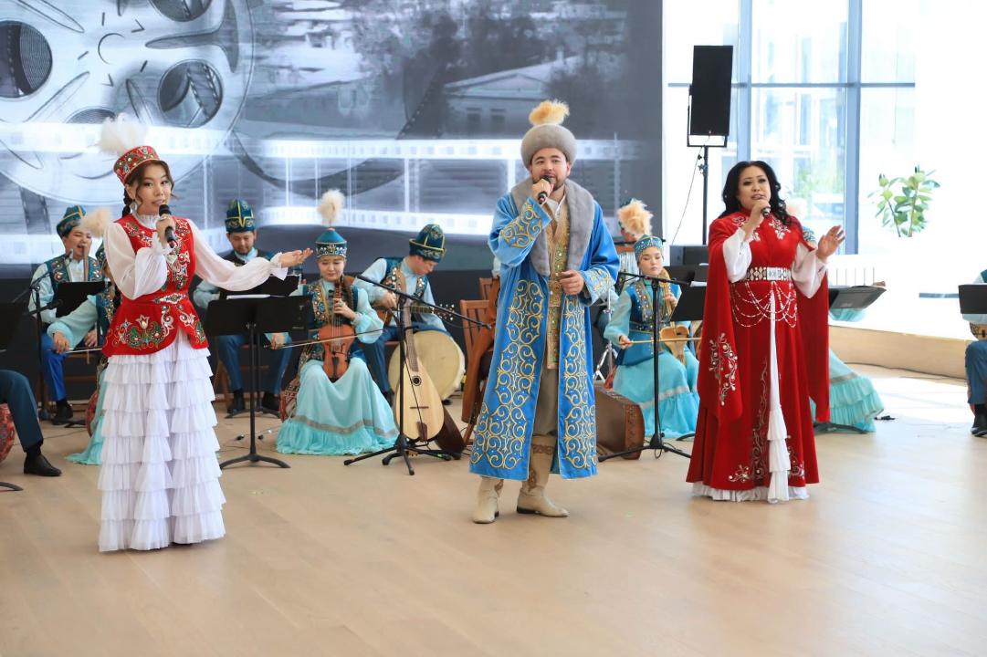 Ұлттық киім киген әншілер мен музыканттардың сахнадағы қойымы.