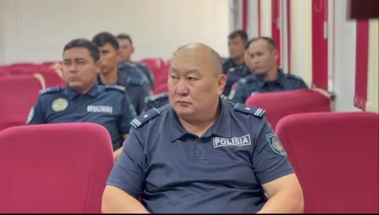 Группа полицейских в темно-синей форме с надписью «POLISIA» сидит в зале на красных креслах.