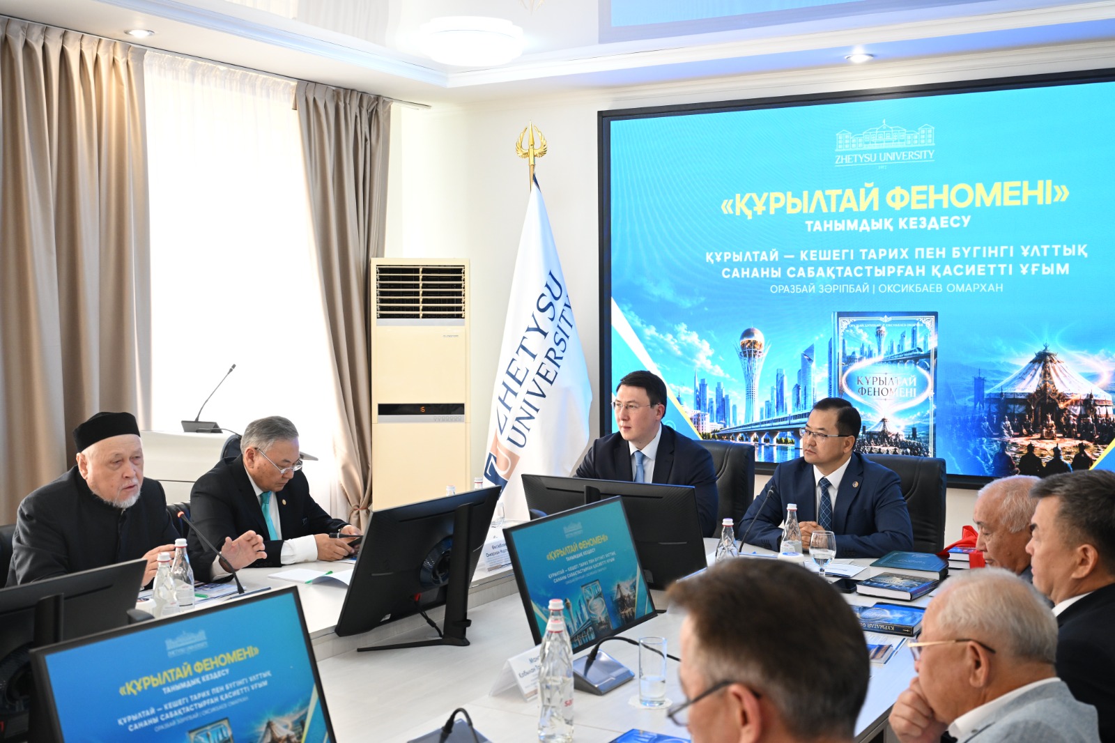 Участники на совещании в Zhetysu University на фоне экрана с презентацией «Құрылтай феномені».