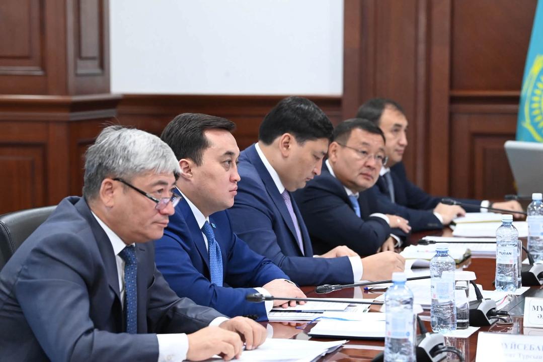 Костюм киген бес ер адам жиналыс үстелінде отыр.