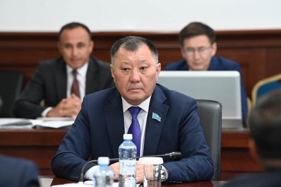 Көк костюм киген ер адам жиналыста отыр.