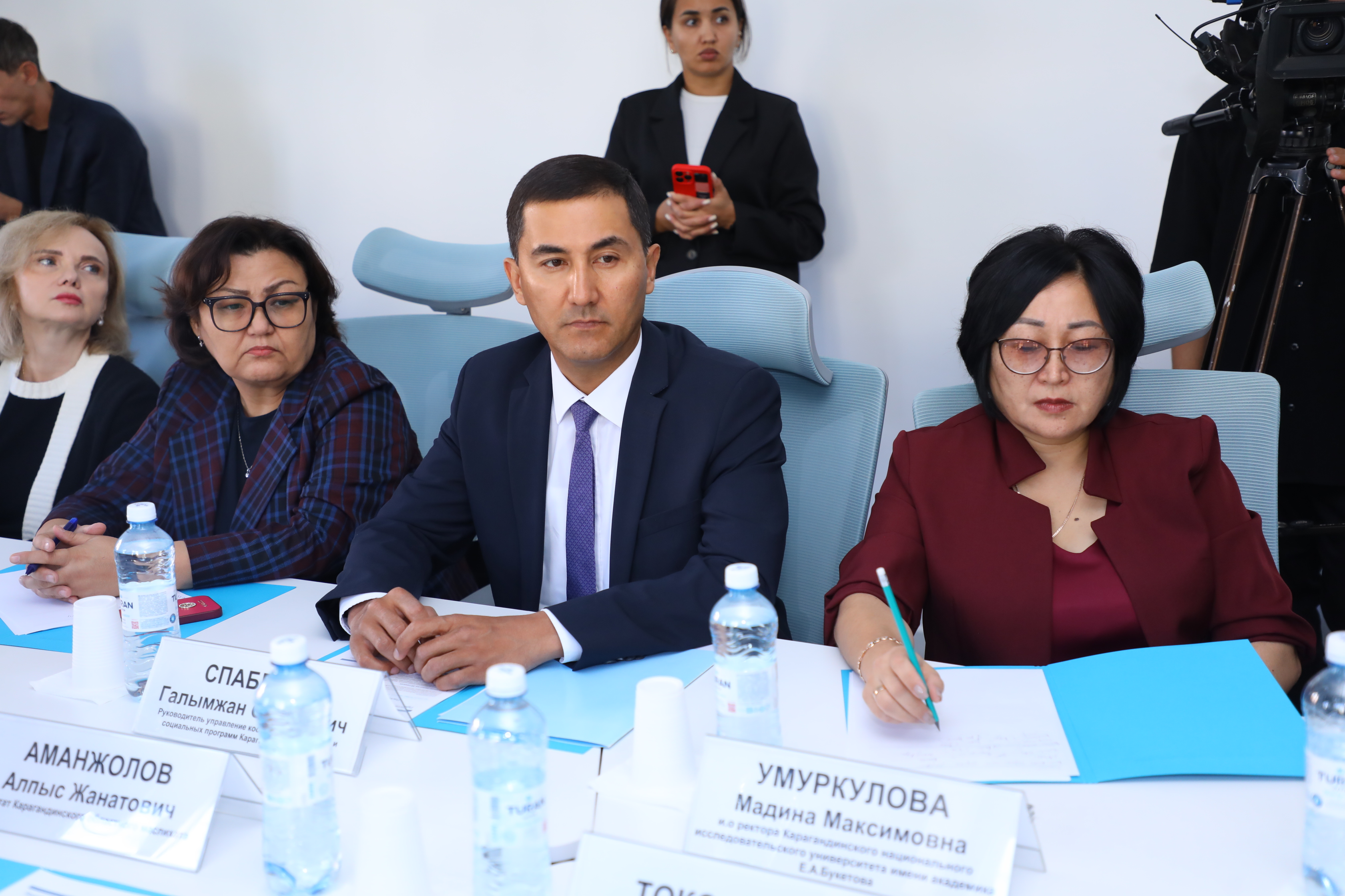 Жиналыста үстел басында отырған ресми киінген адамдар.