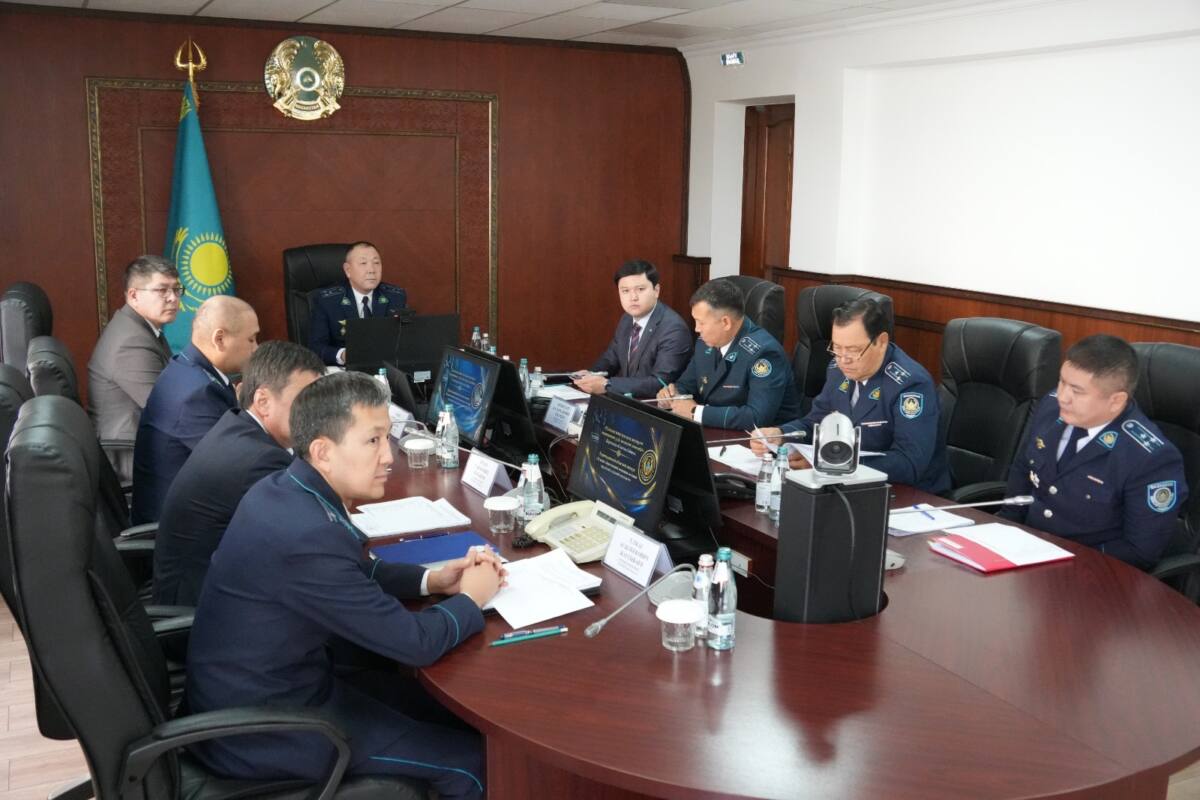 Жиналыс залында үстел басында отырған полиция қызметкерлері мен ресми тұлғалар.