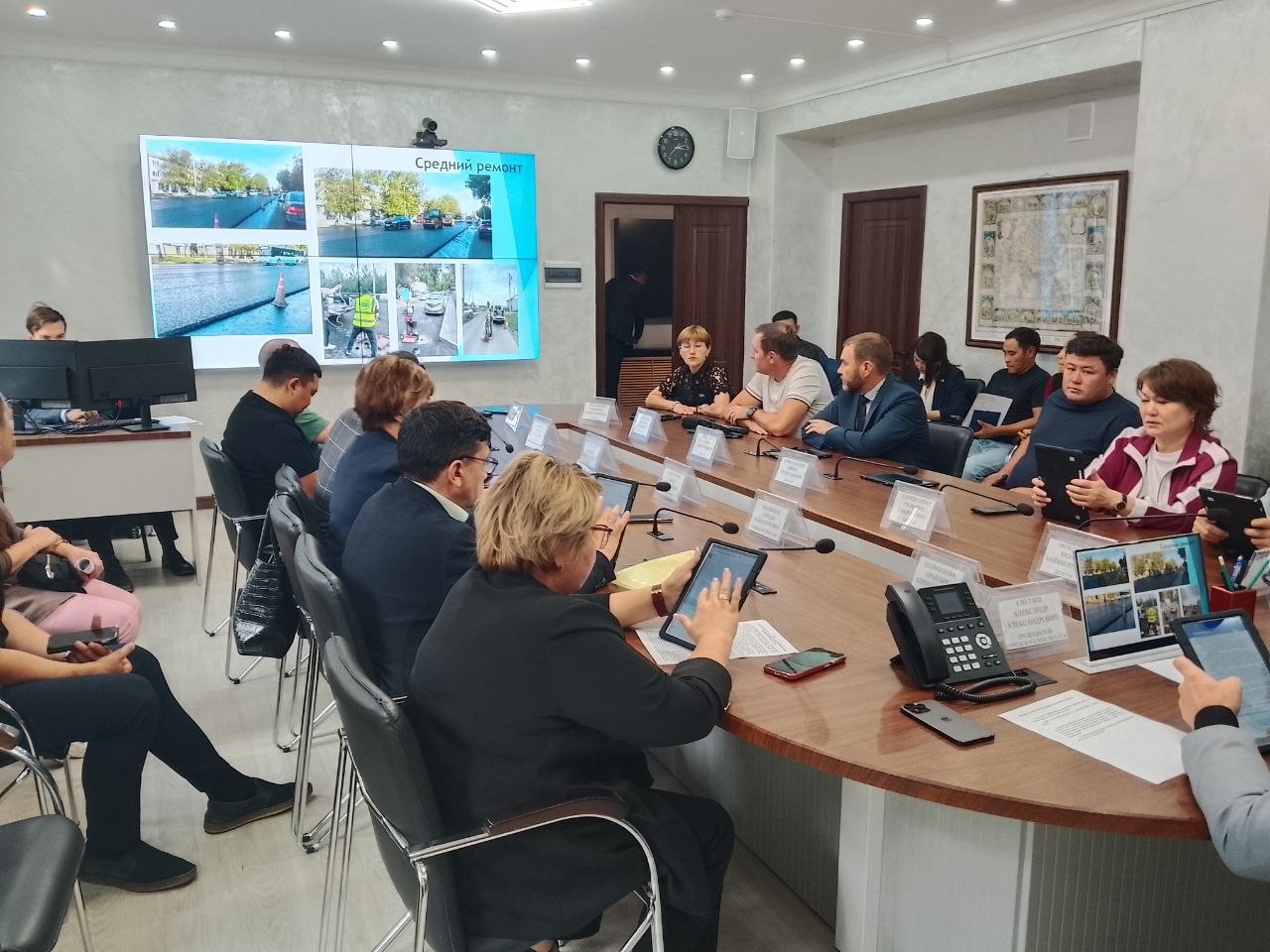 Жиналыс залындағы адамдар презентацияны талқылап отыр.
