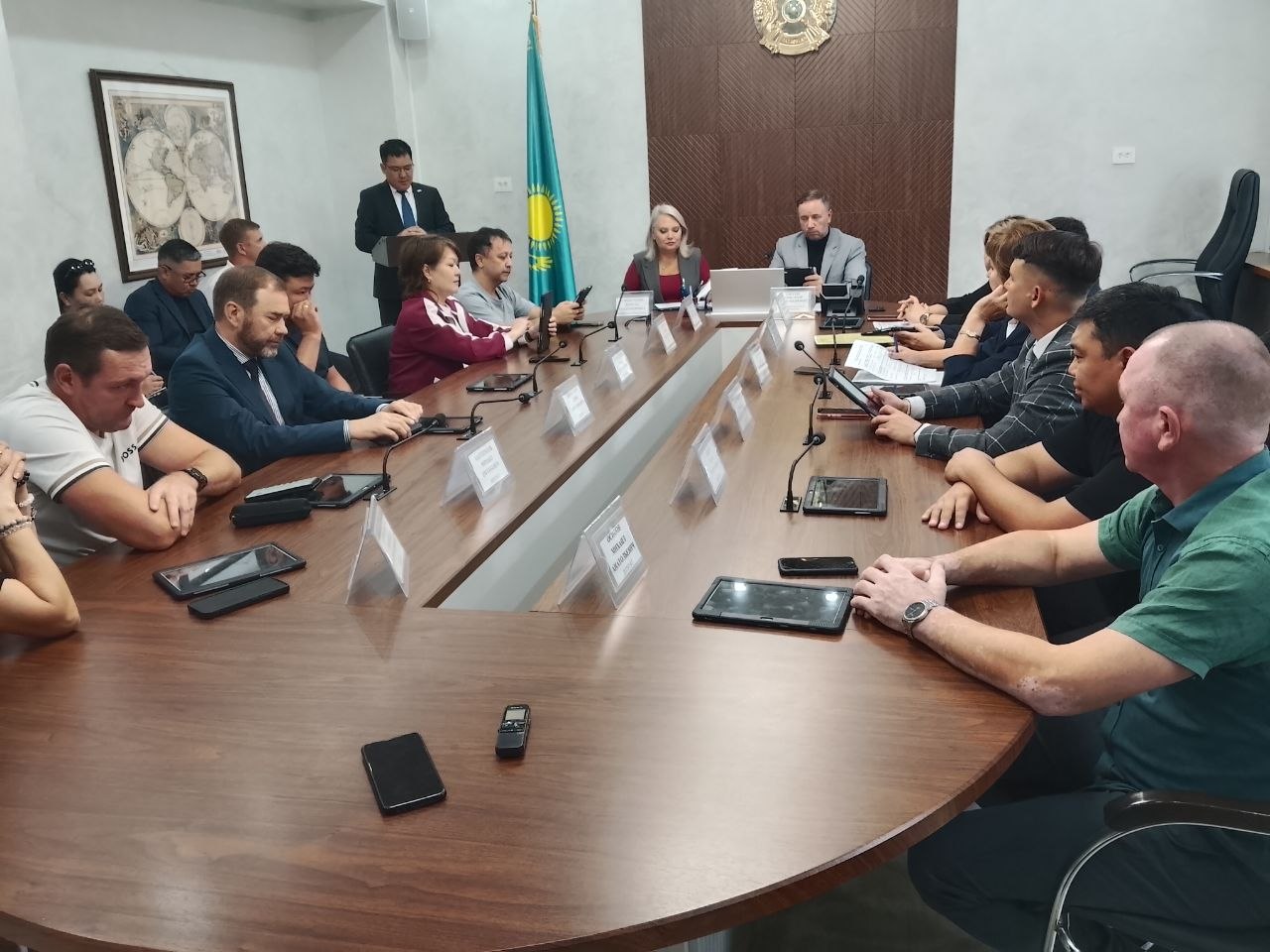 Жиналыс залында үстел басында отырған адамдар тобы.