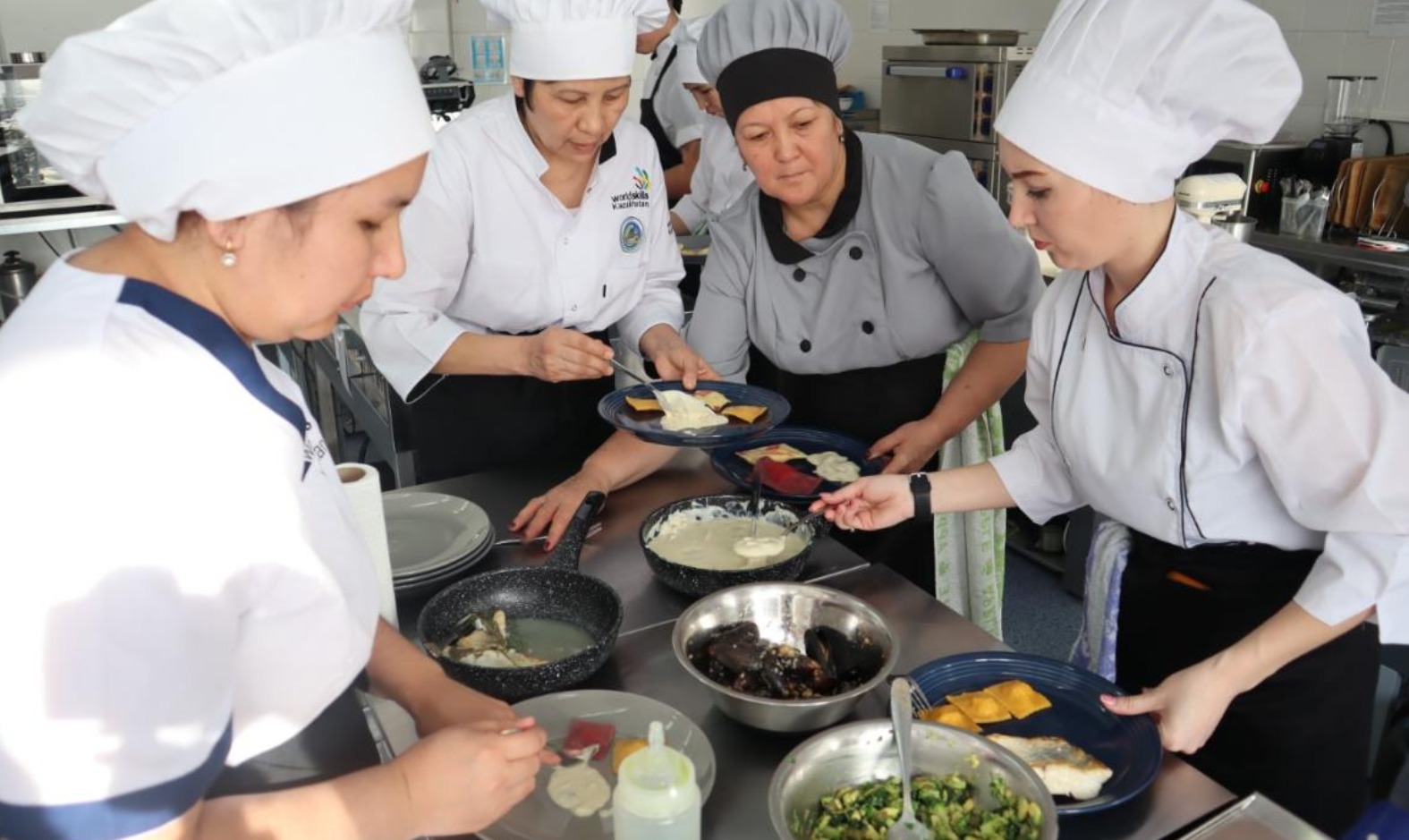 Аспаз киіміндегі төрт әйел асханада тағамдарды дайындап, безендіріп жатыр.