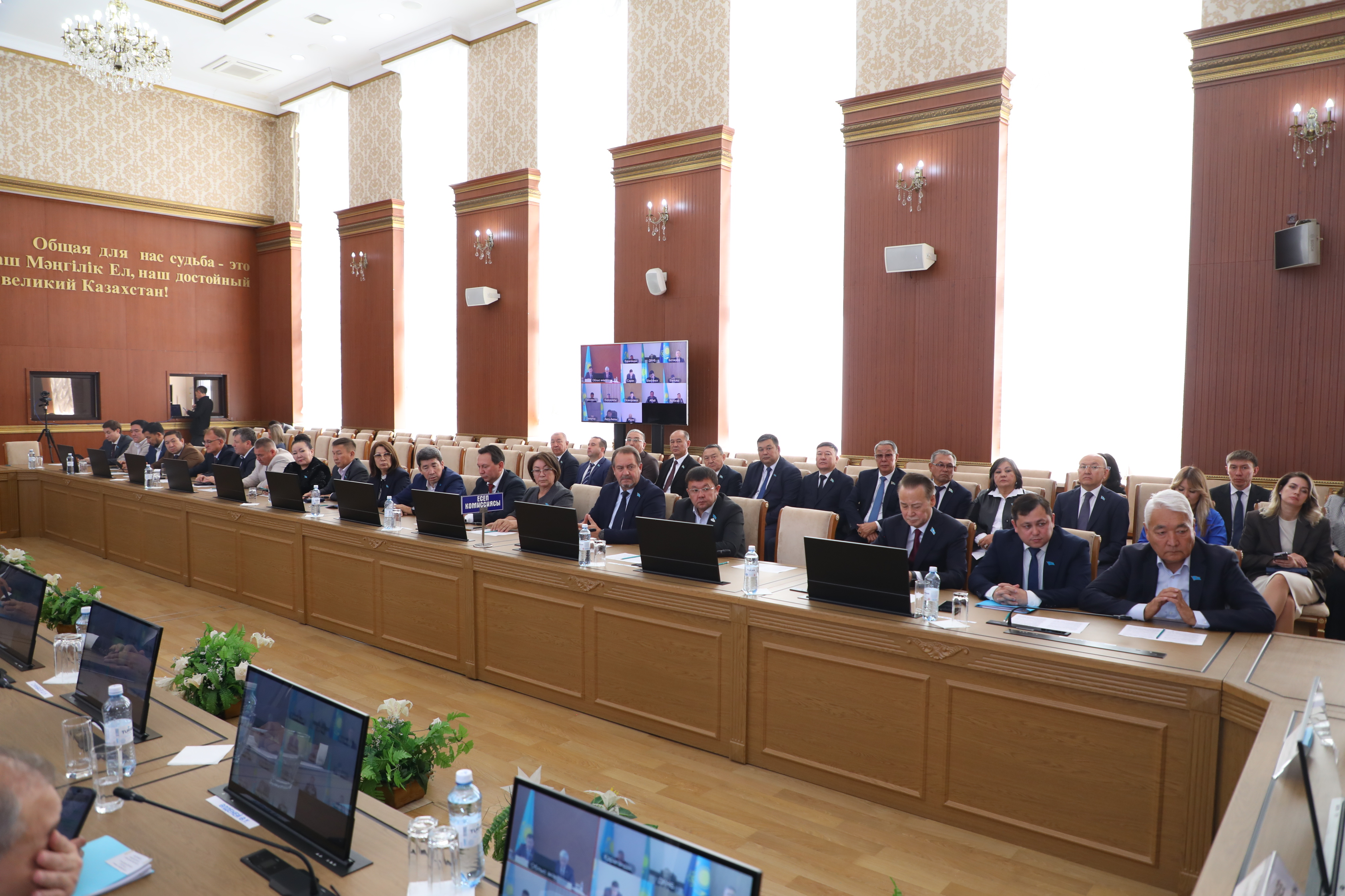 Жиналыс залындағы үстел басында отырған ресми тұлғалар мен ноутбуктер.
