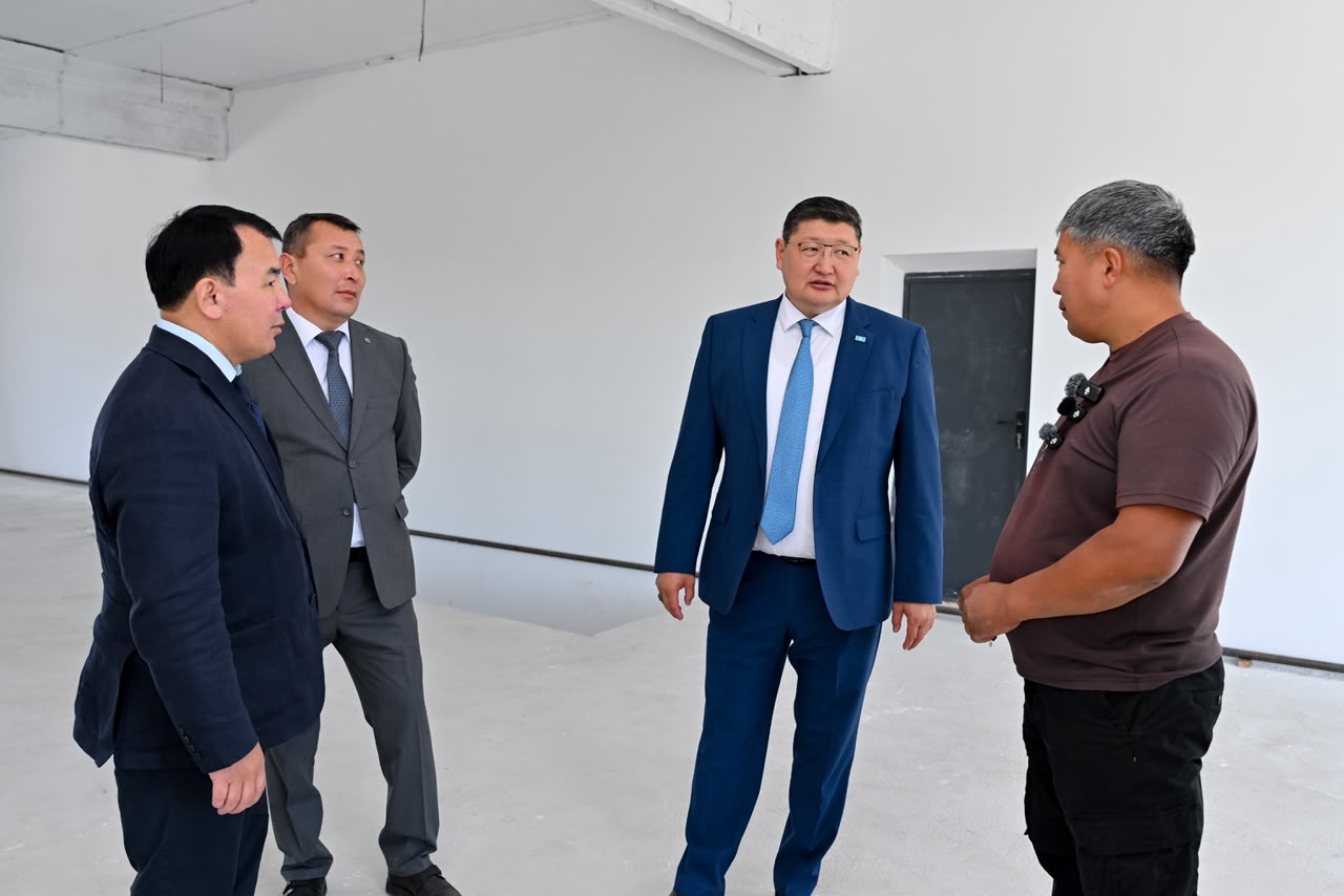 Костюм киген үш ер адам мен қара футболка киген ер адамның ақ бөлмедегі сөйлесуі.