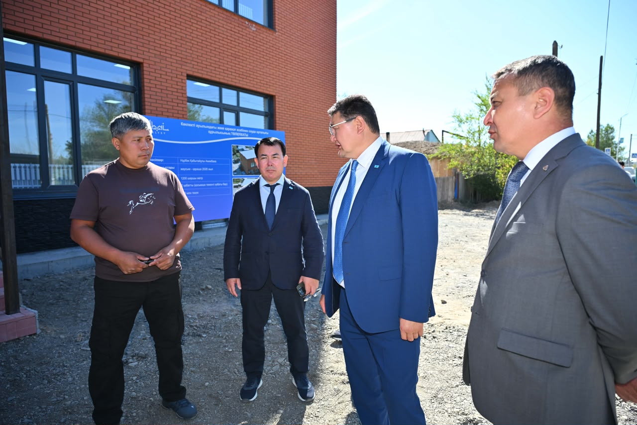 Кірпіш үйдің алдында тұрған төрт ер адам. Үшеуі костюде, біреуі қарапайым киімде.