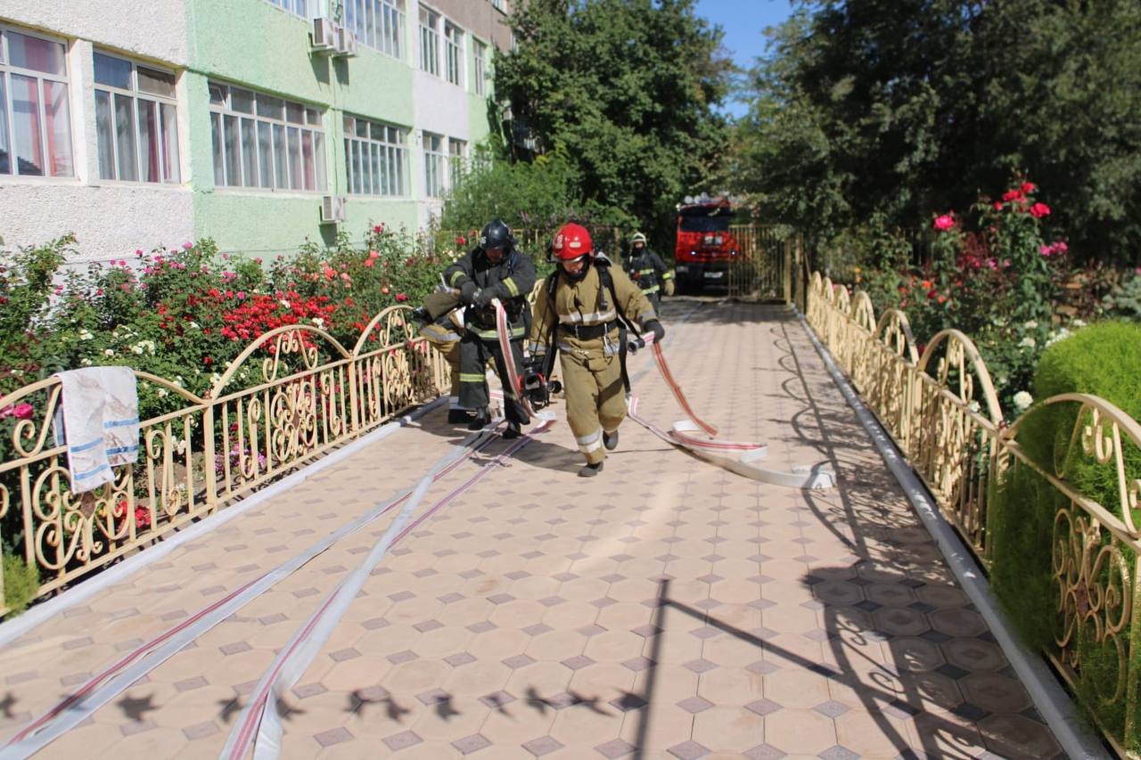 Өрт сөндірушілер ғимарат алдында өрт сөндіру шлангтарын жаюда.