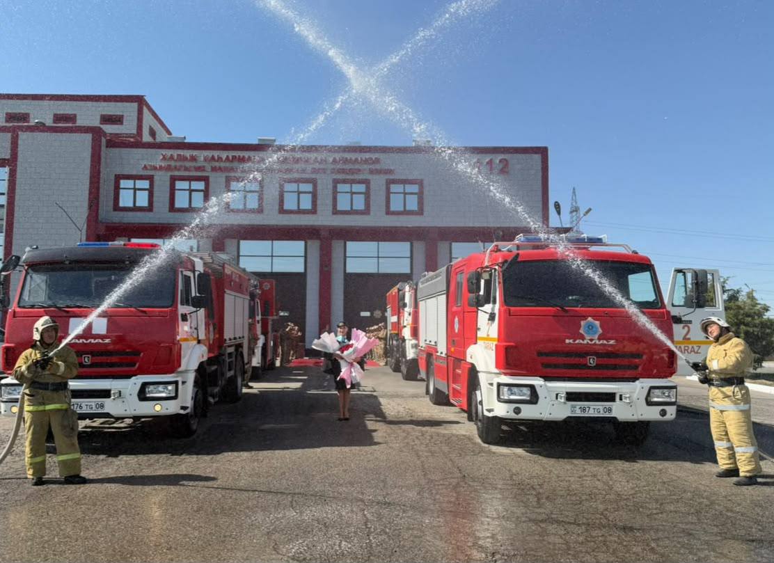Өрт сөндіру станциясы алдында су шашып тұрған екі өрт сөндіру көлігі мен өрт сөндірушілер.
