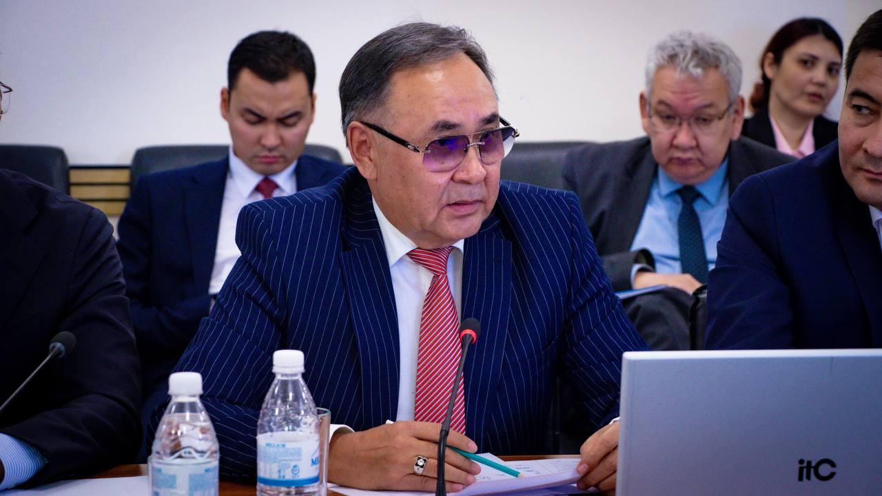 Мужчина в синем полосатом костюме и очках выступает на совещании