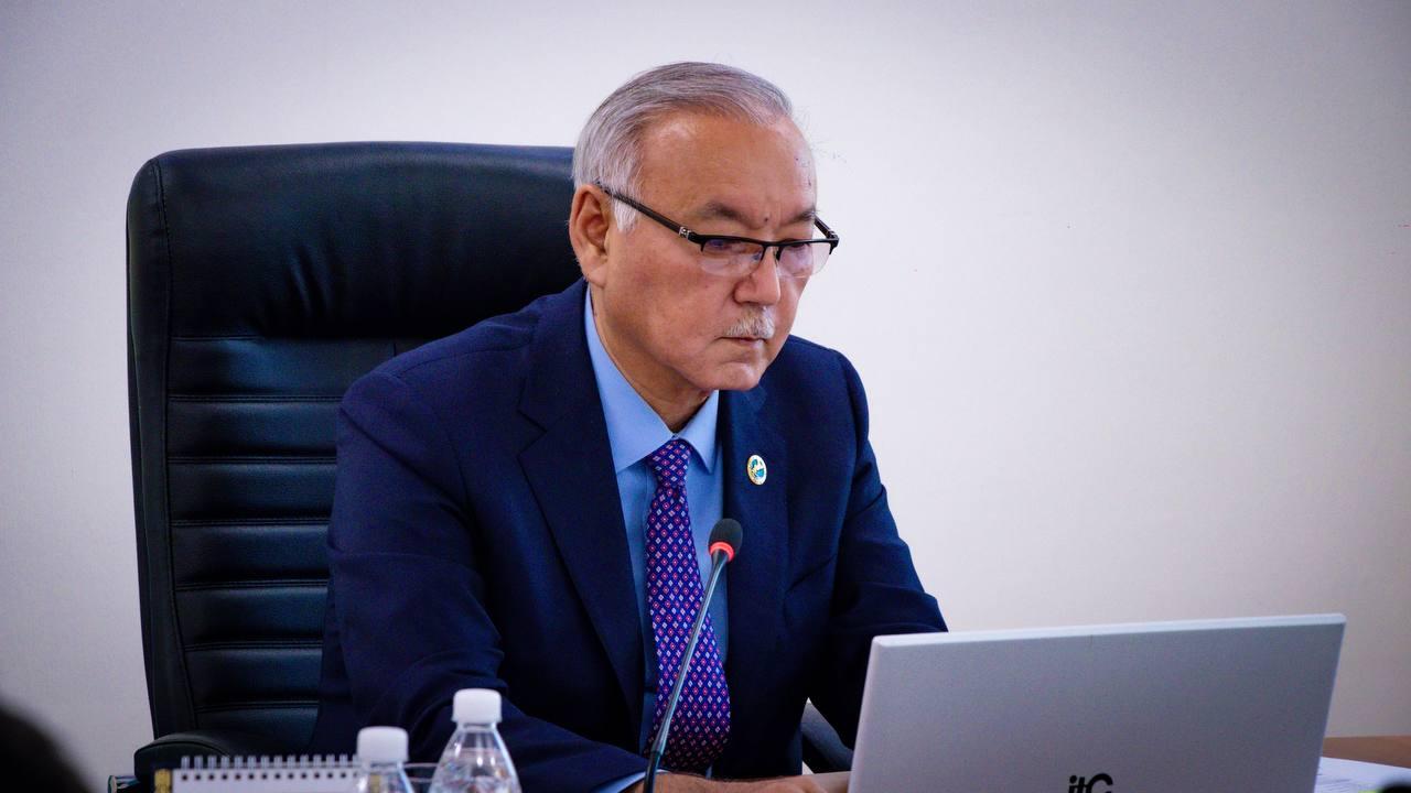 Мужчина в синем костюме и очках работает за ноутбуком, сидя в офисном кресле.