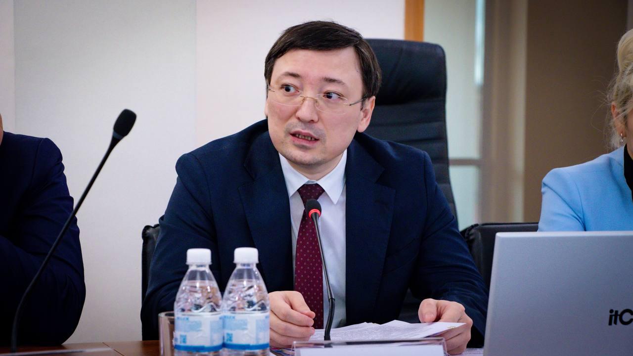 Мужчина в темно-синем костюме и красном галстуке выступает на совещании