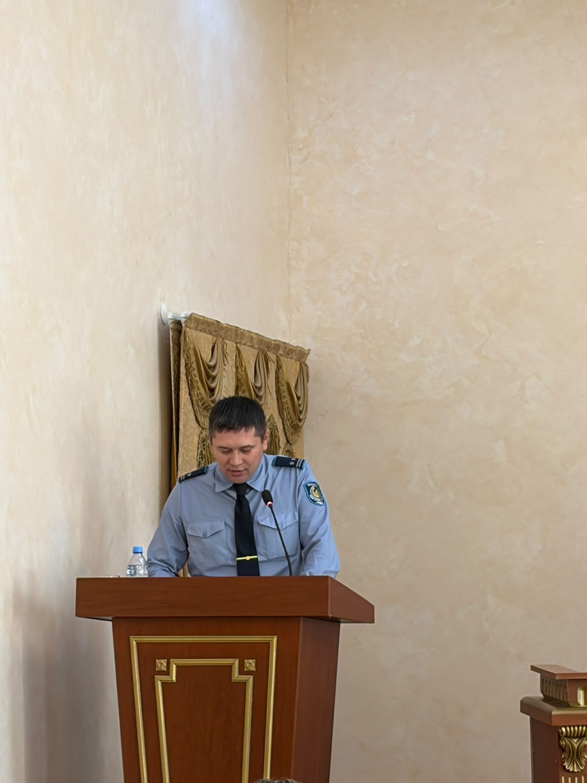 Полиция киіміндегі ер адам ағаш мінбеден шығып тұрады.