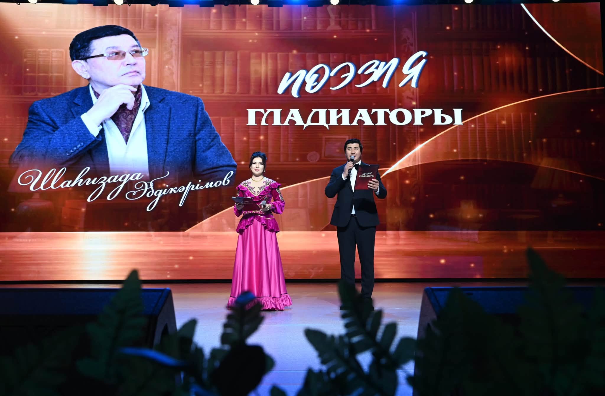 Сахнадағы жүргізушілер және артқы фондағы «Поэзия гладиаторы» жарысының суреті.