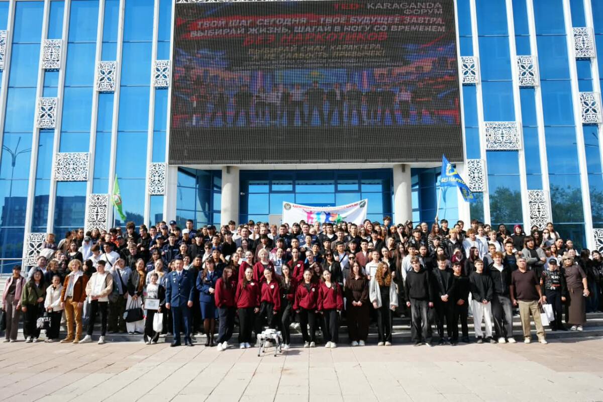 Заманауи ғимарат алдында жиналған үлкен студенттер тобының ұжымдық суреті.