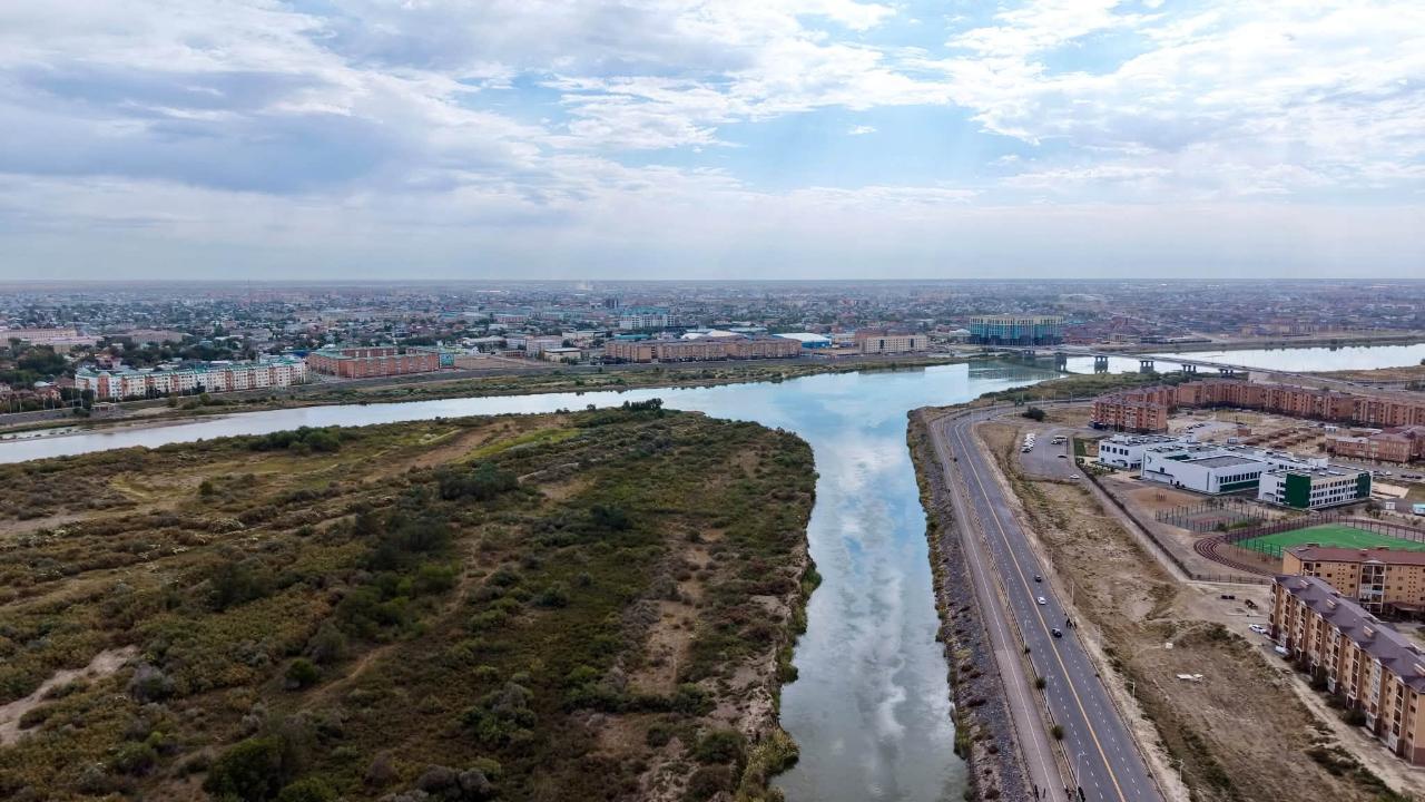 Қала көрінісі: өзен, жол және тұрғын үйлердің жоғарыдан түсірілген панорамасы.