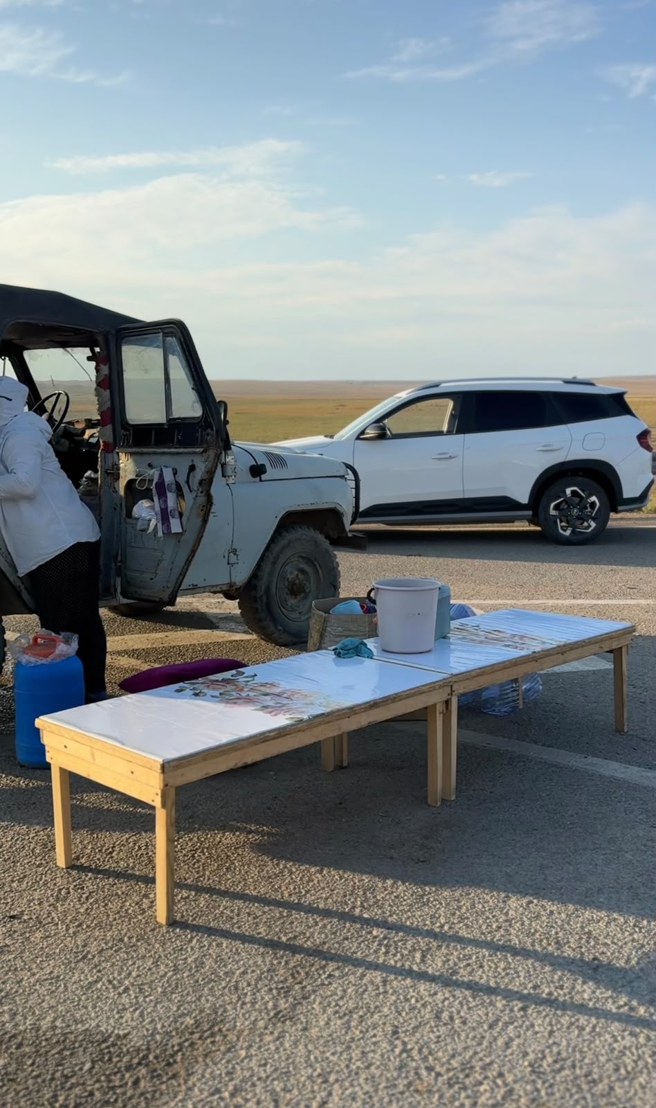Жол жиегіндегі ақ үстел, ескі жол көлігі және ақ түсті заманауи кроссовер.
