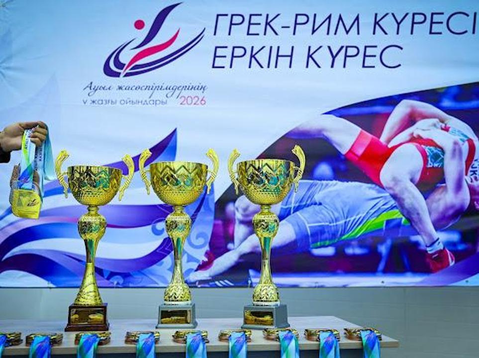Күрес жарысының алтын кубоктары мен медальдары. Фонда «Грек-рим және еркін күрес» жазуы бар баннер.