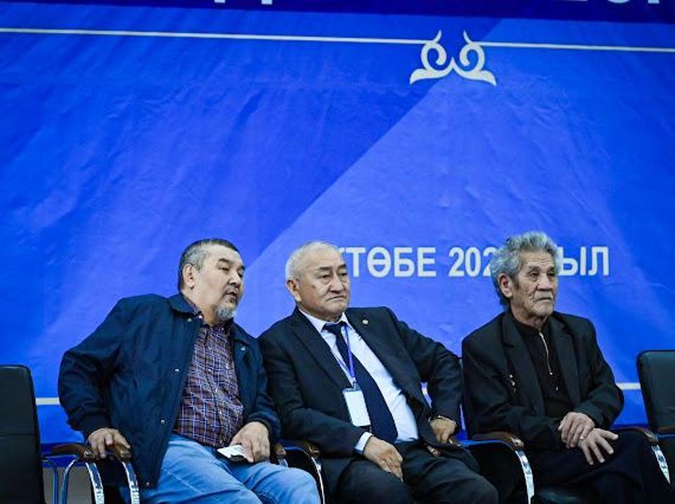 Көк түсті фон алдында отырған үш ер адам.