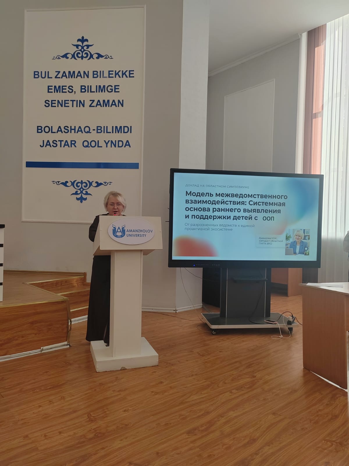 Amanzholov University-де баяндама жасап жатқан спикер және презентация экраны.
