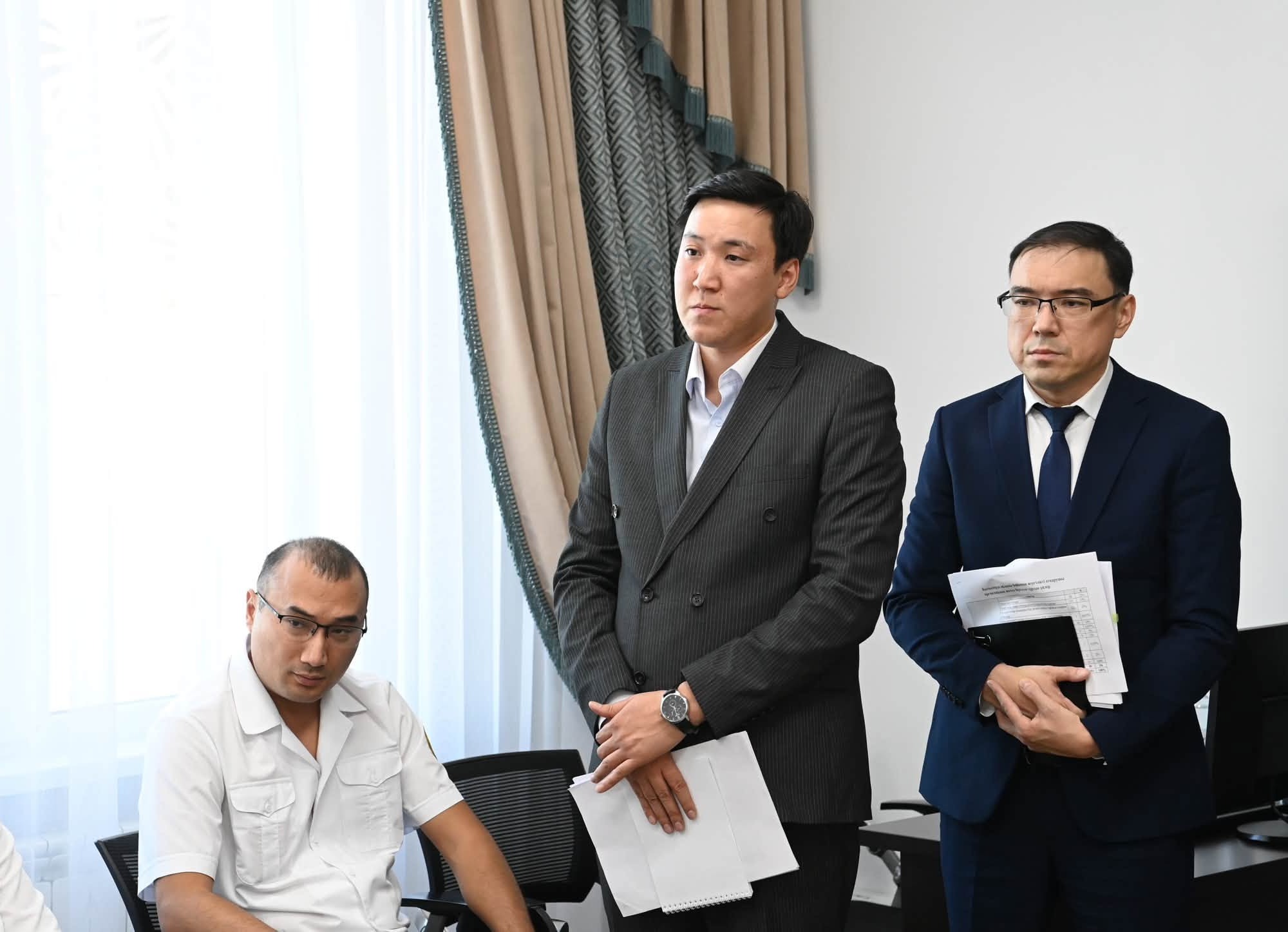 Костюм киген екі ер адам және ақ жейделі ер адам тұр.